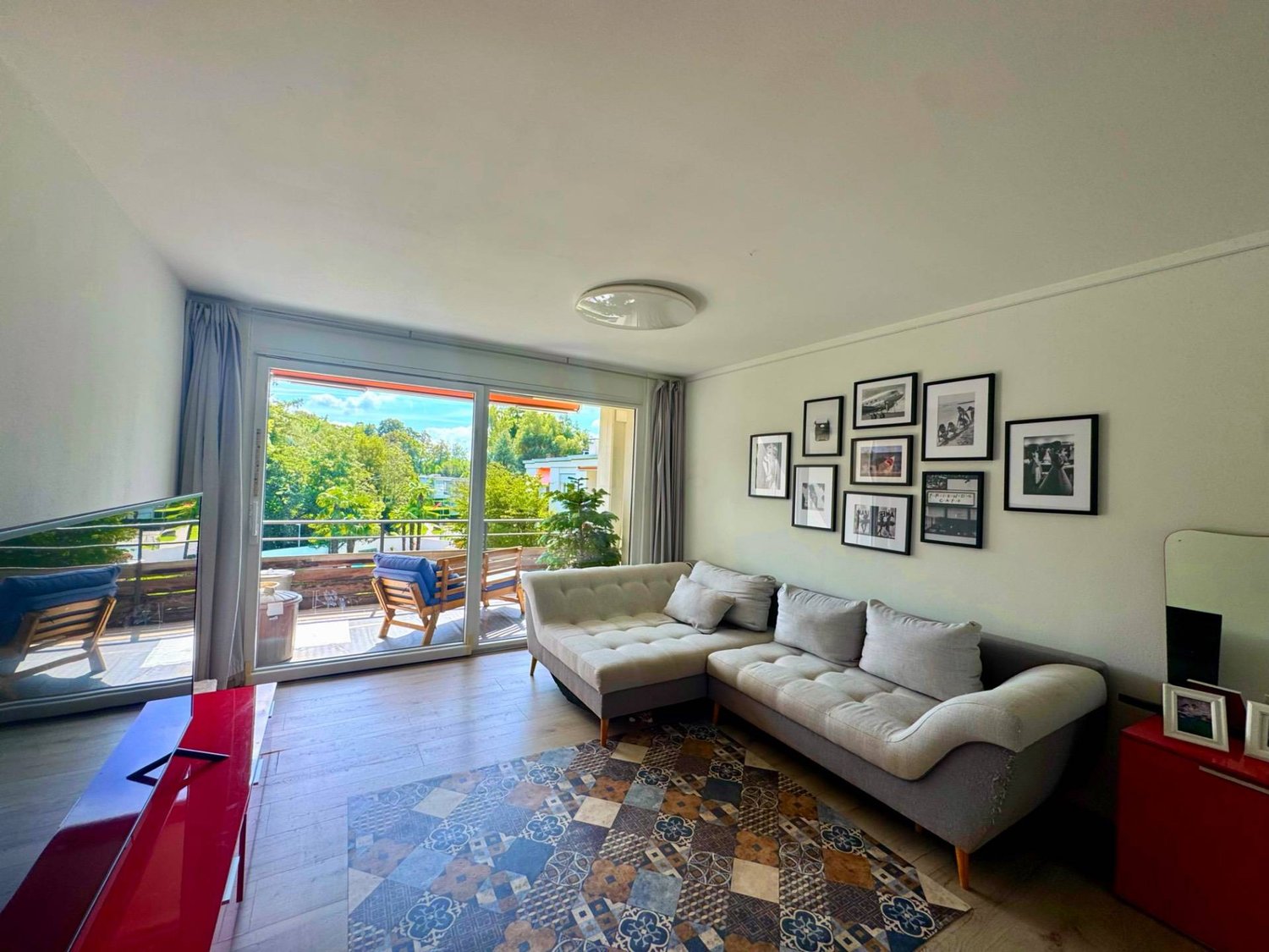 modern apartment living room, L-shaped couch, carpet, floor to ceiling windows, large balcony, trees view