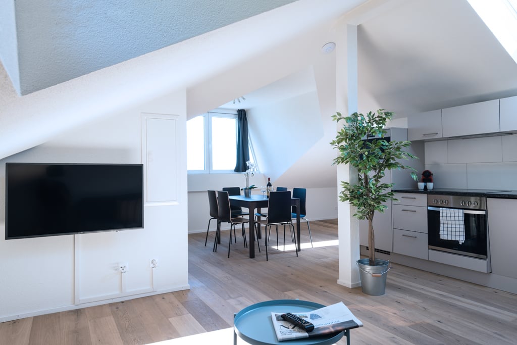 Open-concept living space with living room, dining area, and kitchen. Hardwood floors, large windows, modern kitchen appliances including a dishwasher, and a potted plant for decor.