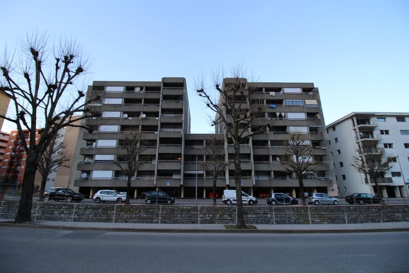 Apartment building with multiple parking spots in front, multiple floors, trees in front