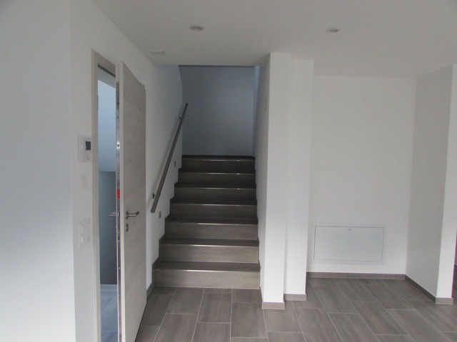 staircase with metal handrail, white walls, tiled floor, open door