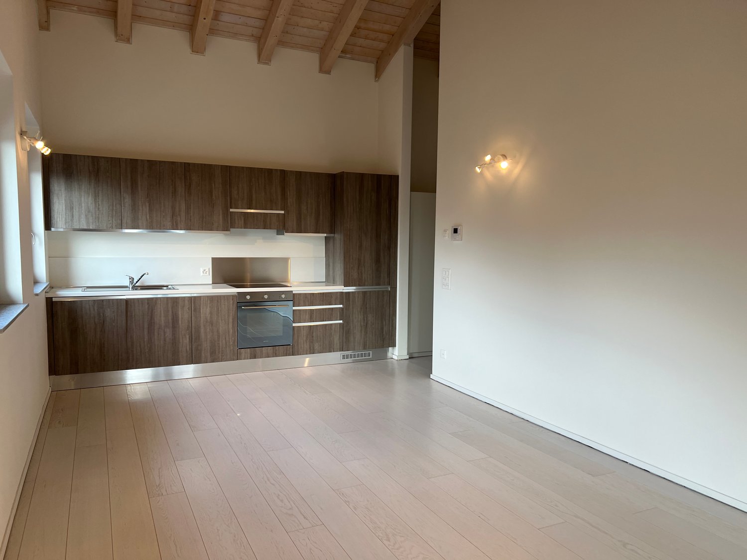 wooden cabinets, white countertops, modern stainless steel oven, sink with faucet, white walls, hardwood floors