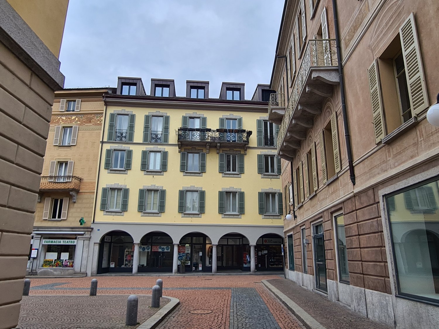 yellow building, 5 stories, many windows, arched doorways, balconies, brick paving