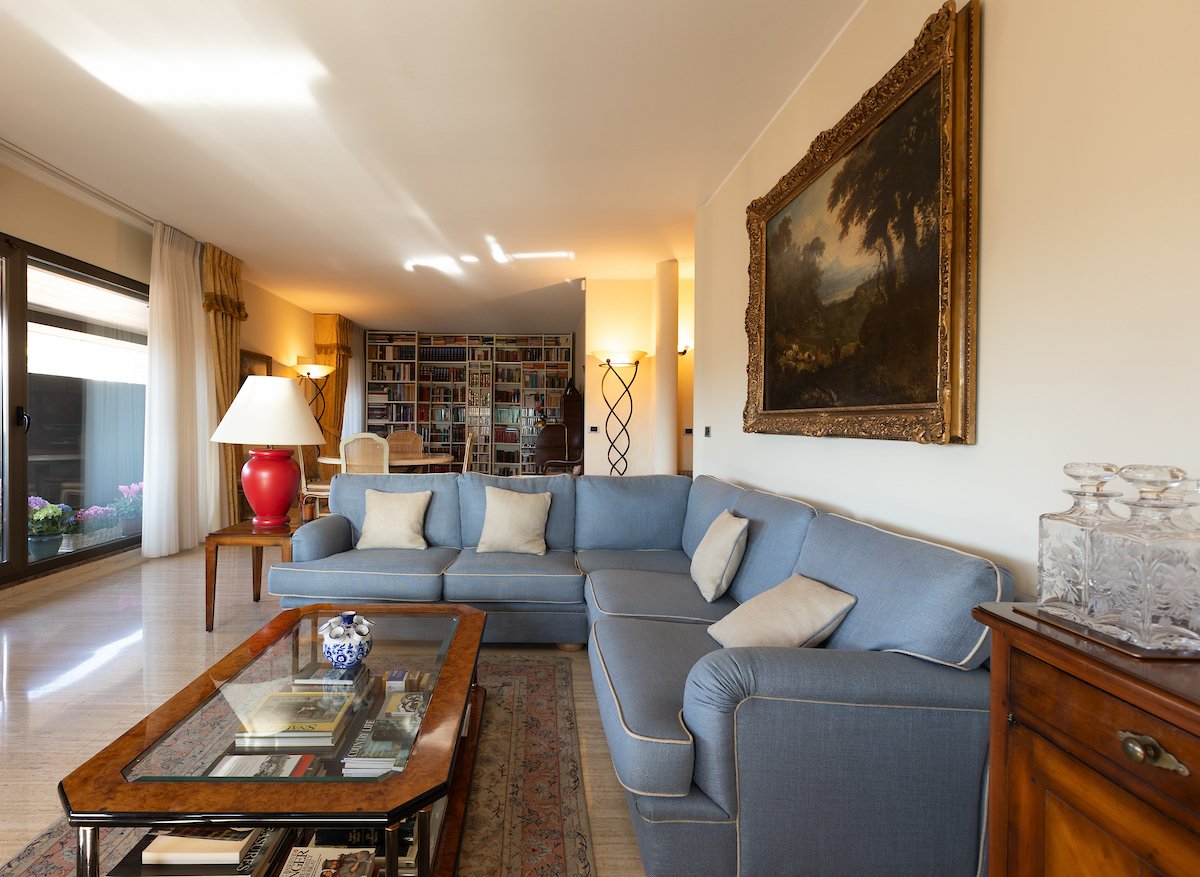 large blue sofa, glass coffee table, wooden cabinet, bookshelves, large window, painting