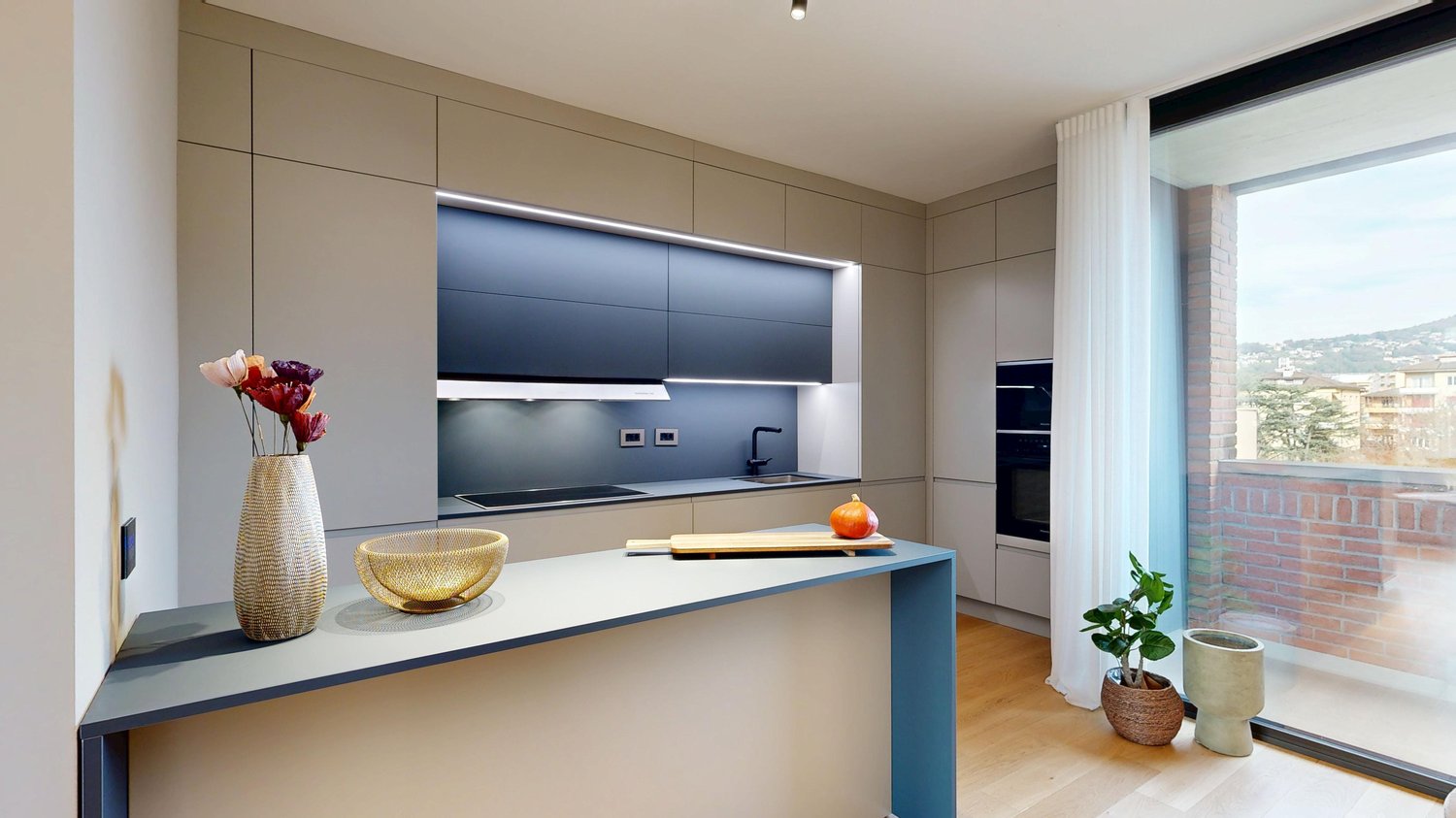 Modern kitchen with beige cabinets, dark blue countertops, built-in appliances, and a large window overlooking a balcony or terrace.