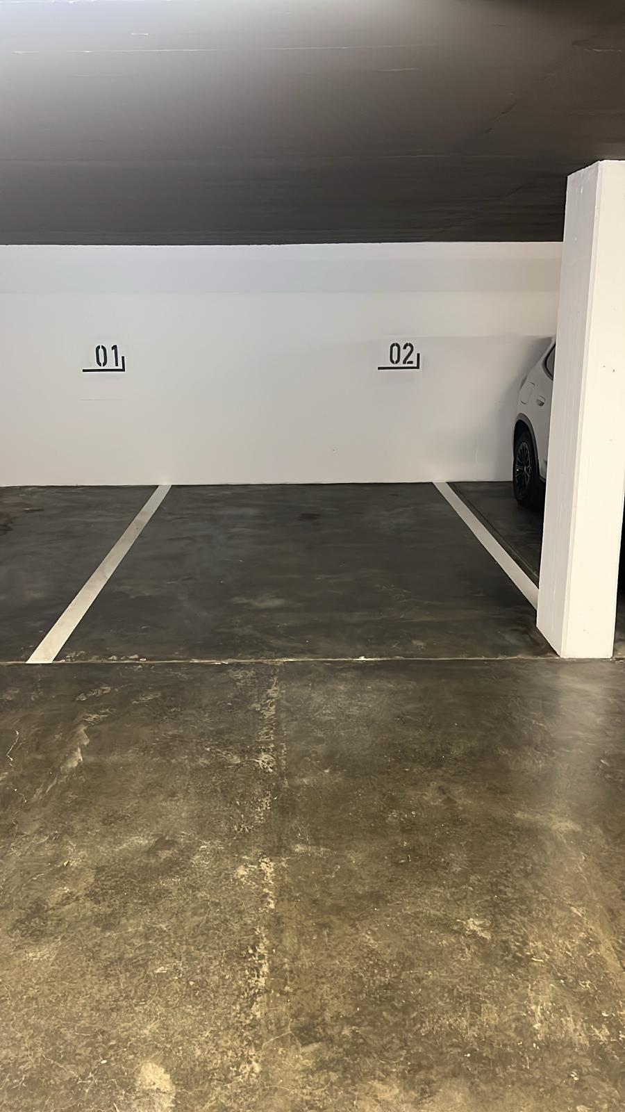 Underground parking lot with two parking spaces, white walls, grey floor, and white pillars