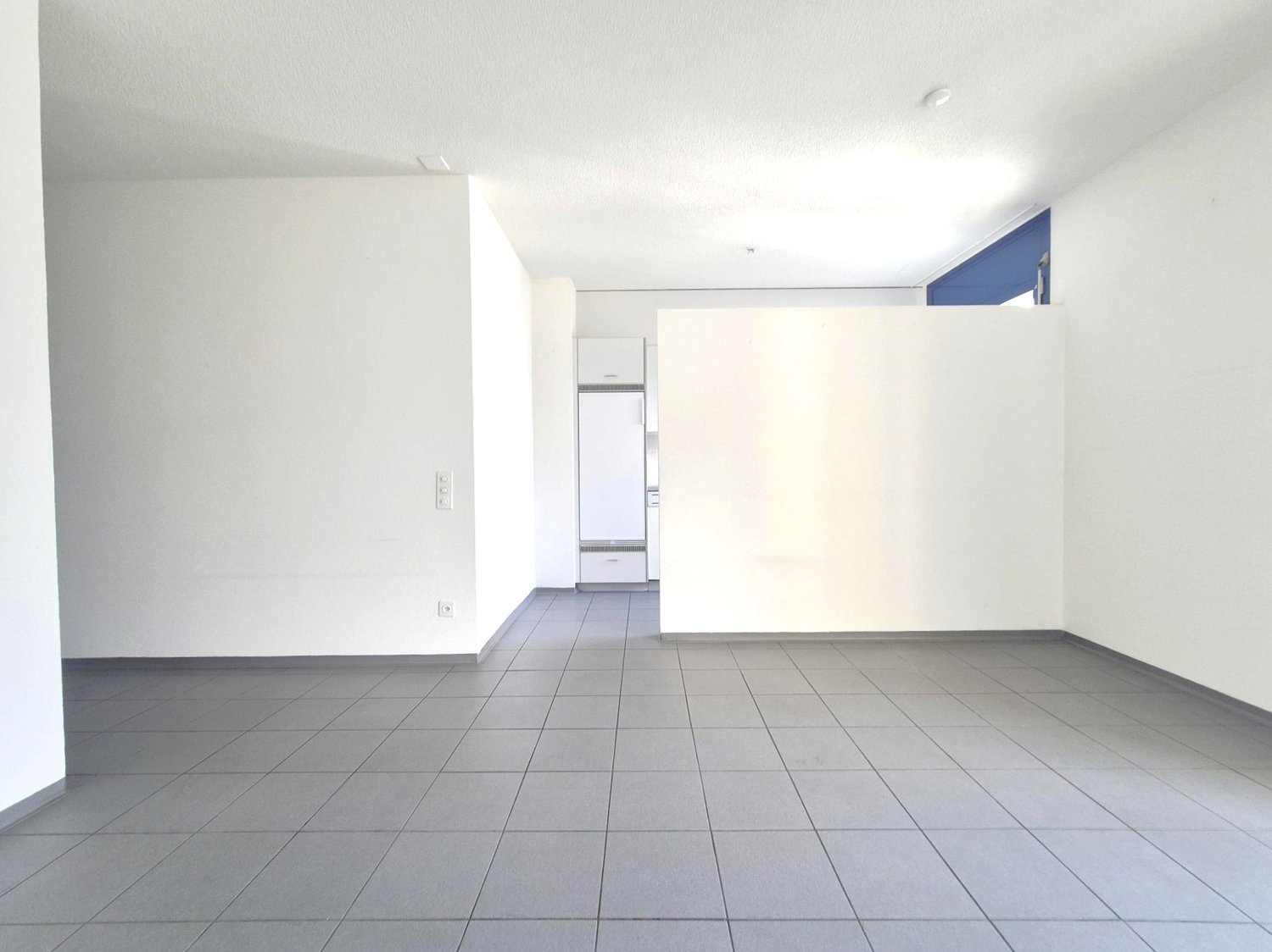 empty room, gray tile flooring, white walls, electrical outlets, white refrigerator in another room