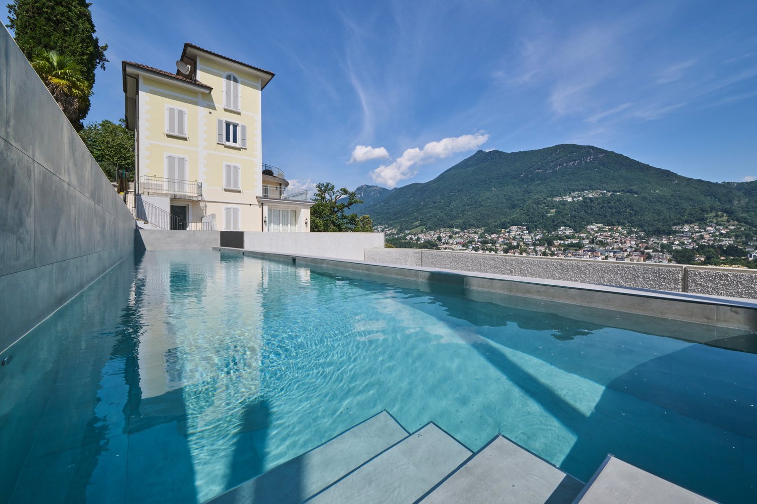 Large swimming pool with tiled flooring, set against the backdrop of a scenic mountainside.