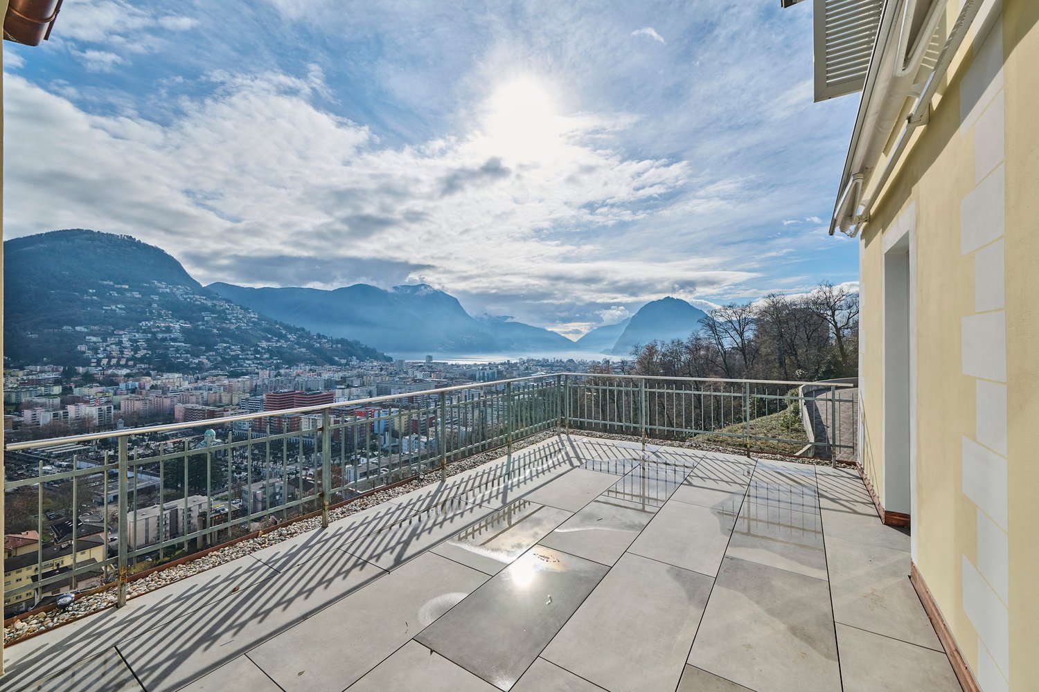 large balcony with tiled floor, metal railing, view of mountains and city