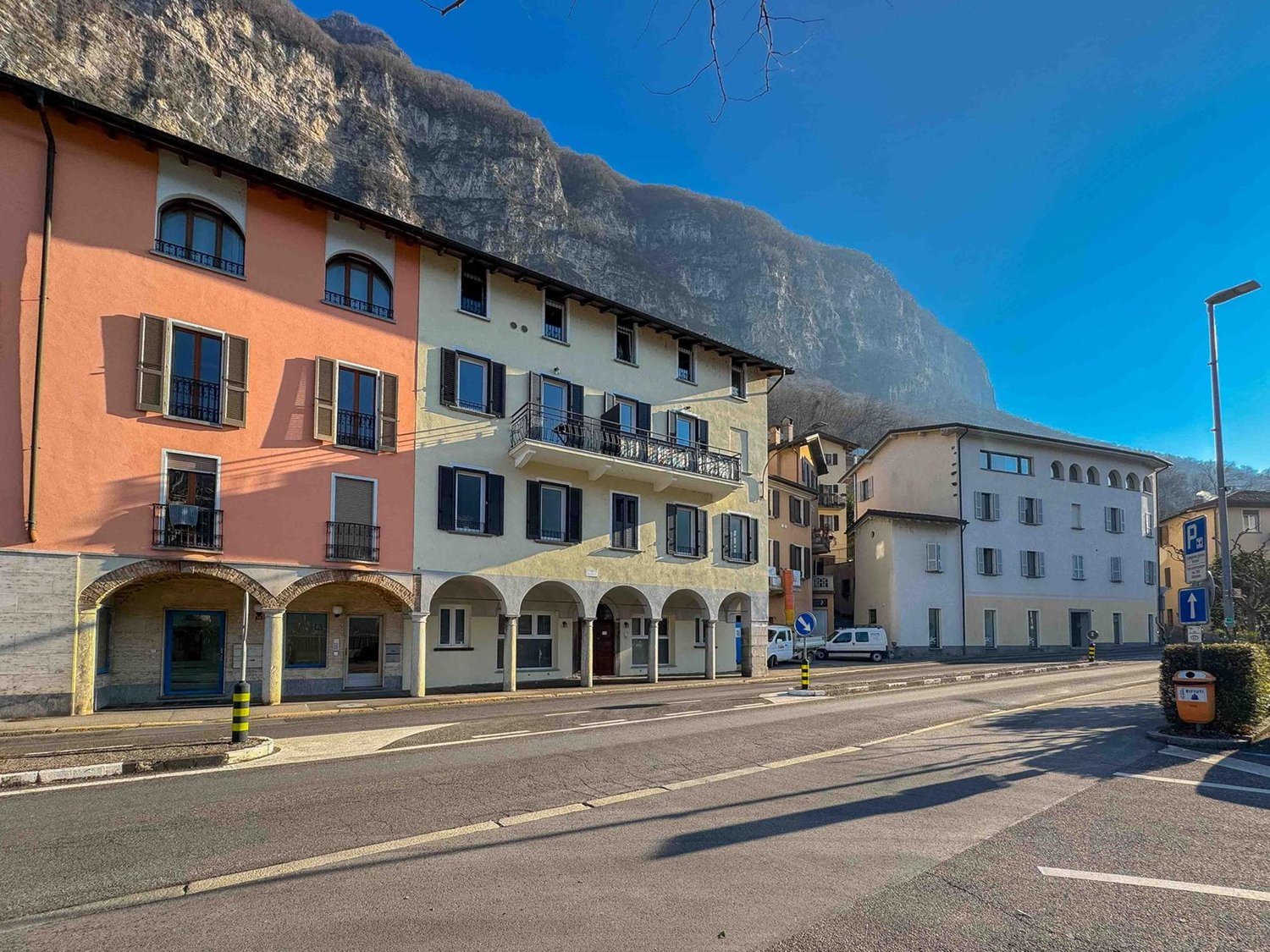 Three story building with balconies, located on a street with a mountain in the background