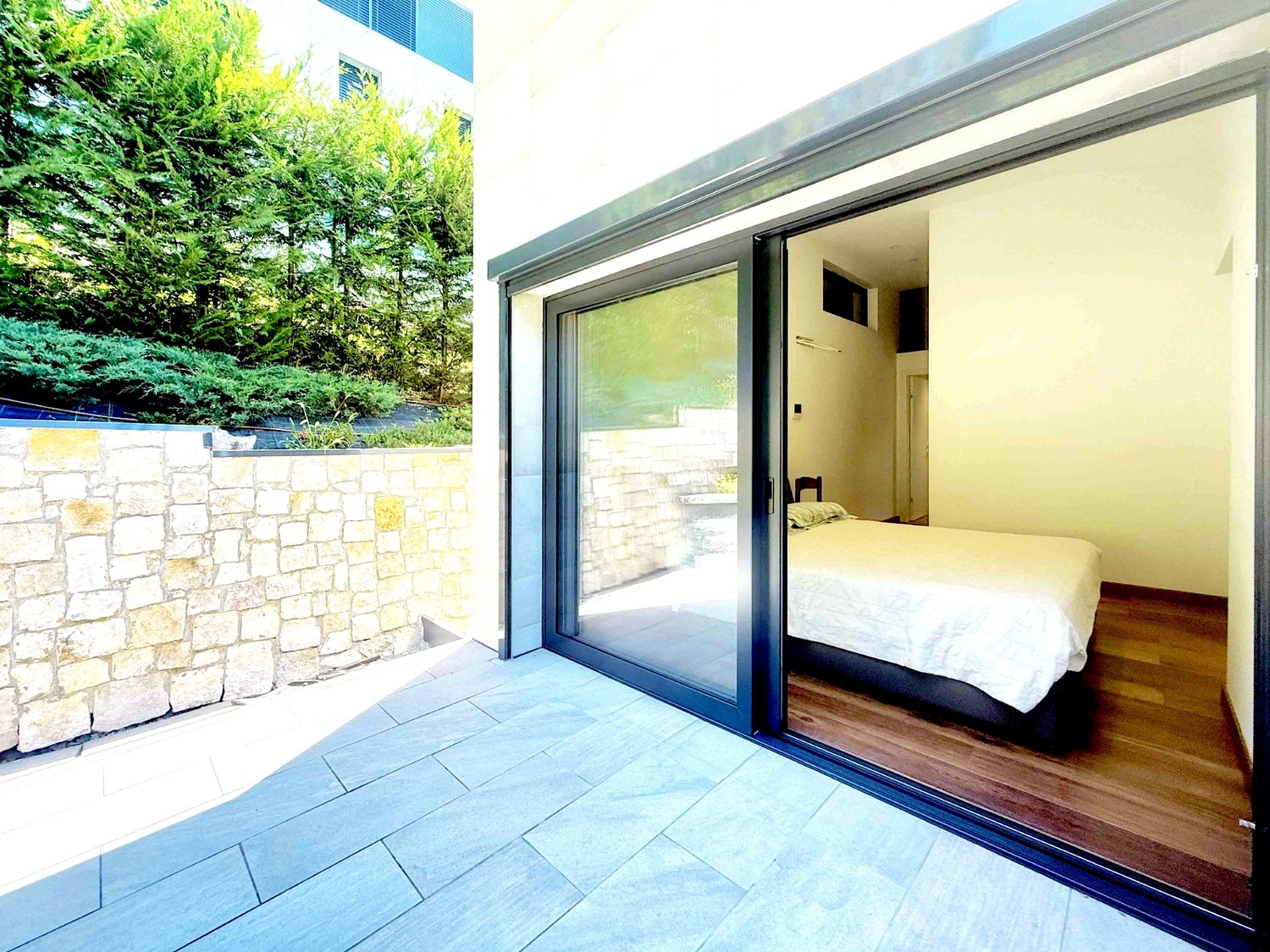 bedroom with bed, sliding glass door, wooden floor, stone wall, outdoor view