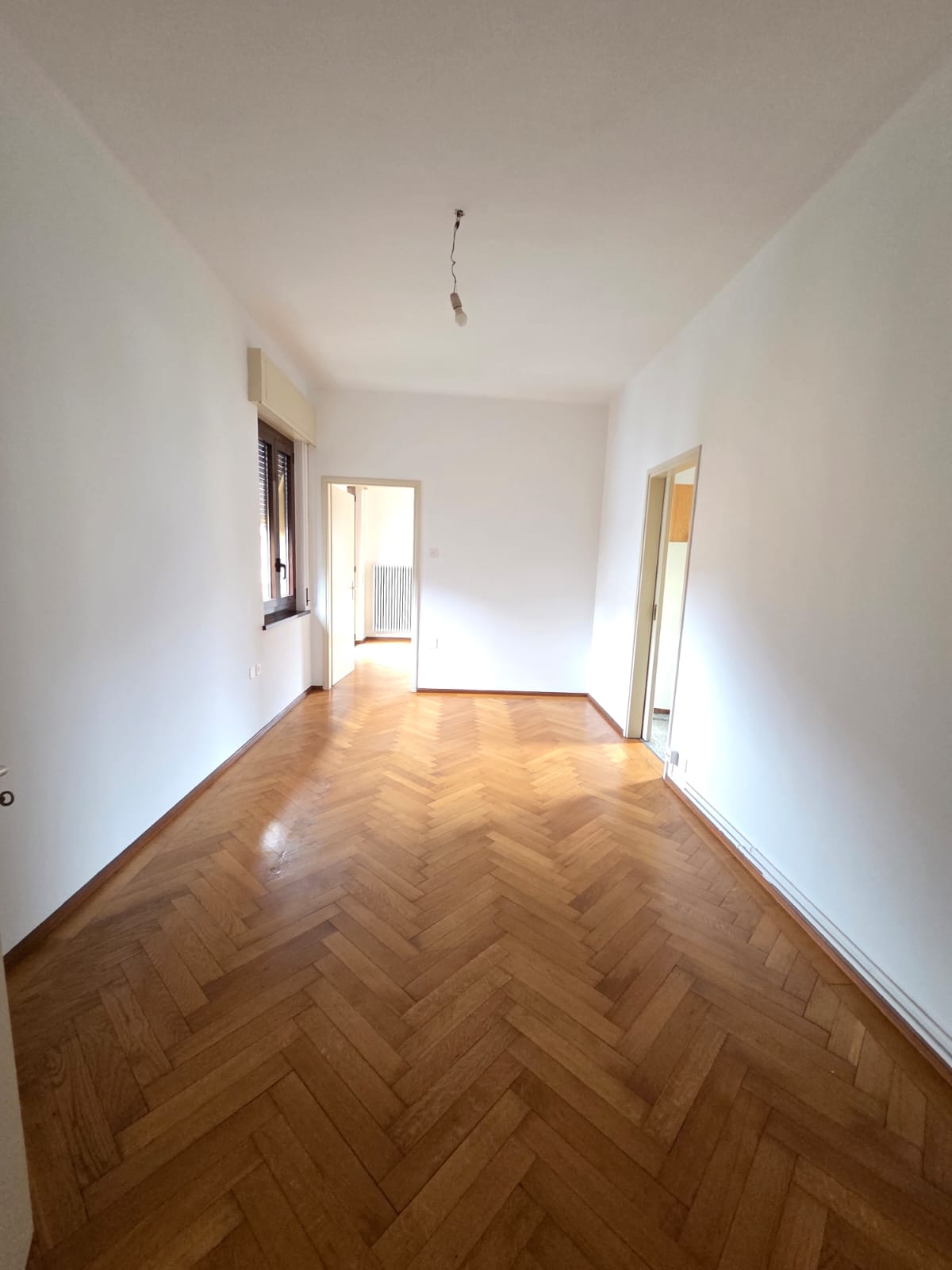 wide empty room, wooden parquet flooring, white walls, window, two doorways