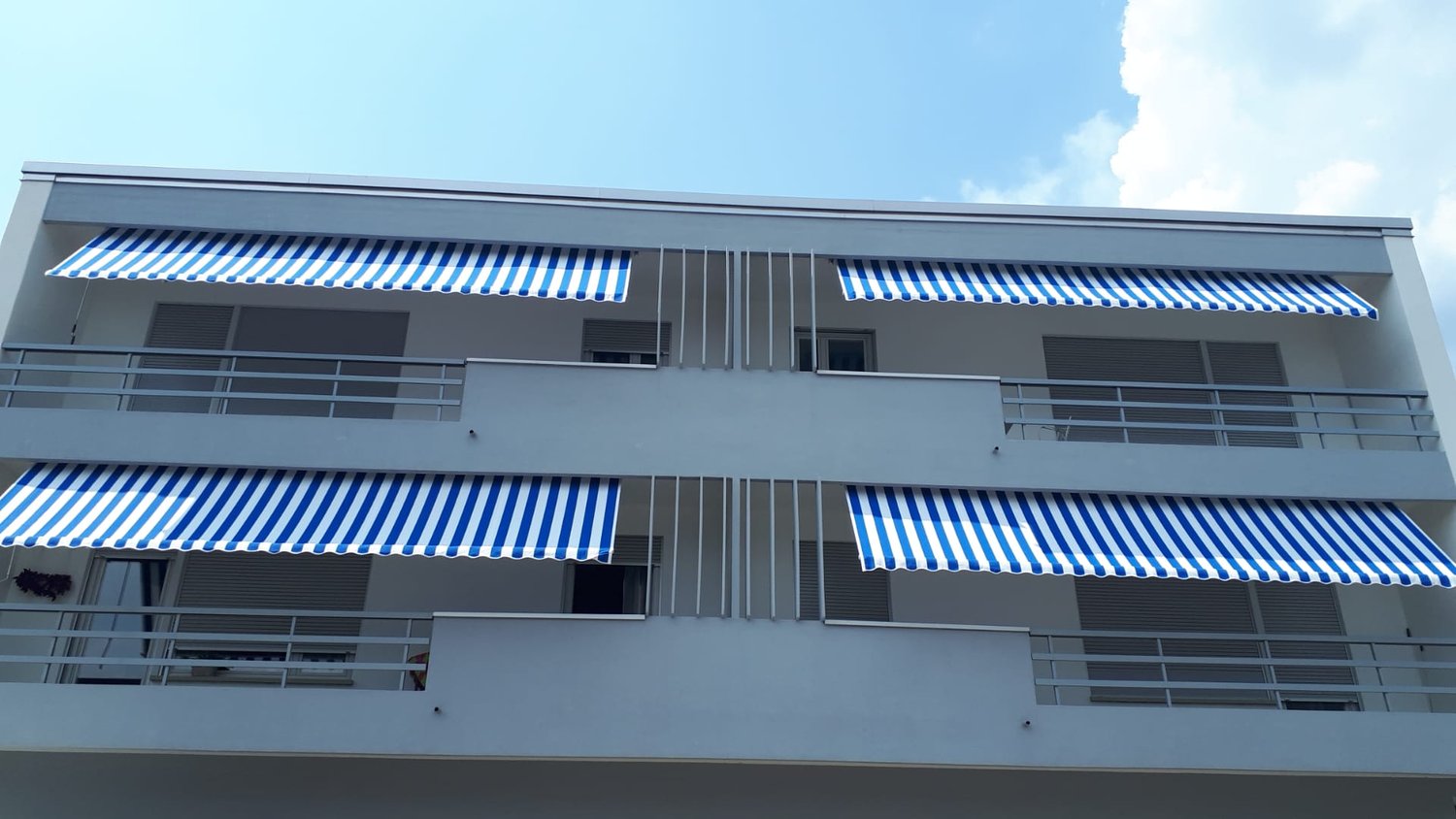 Multi-story building with gray exterior, large windows, and blue and white striped awnings covering the balconies on each floor.