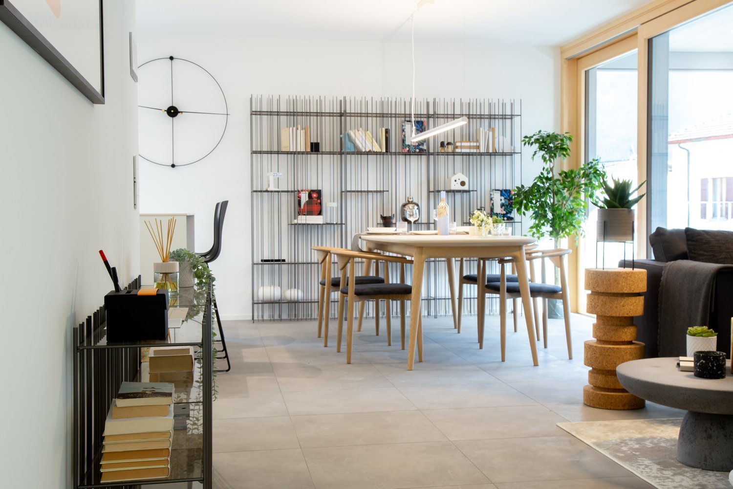 Modern interior with dining table, chairs, shelves with books, plants, and decor items.
