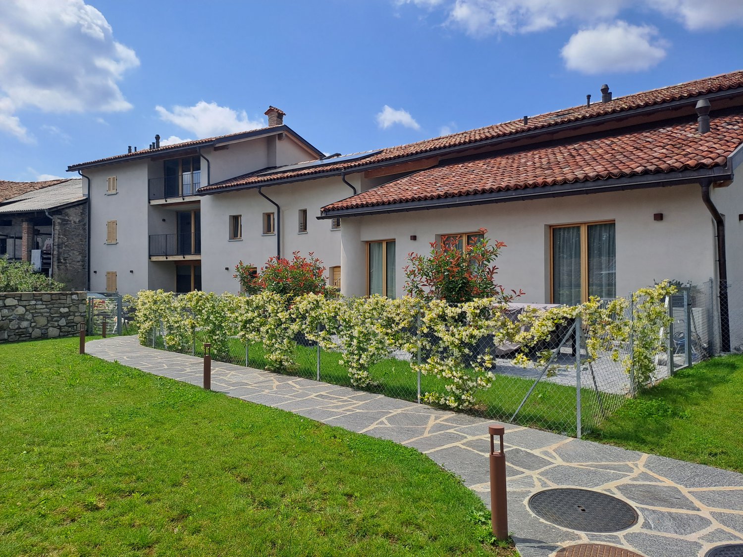 Apartment building with terrace, solar panels, chimneys, garden, walkway, green grass, stone wall, metal fence, plants