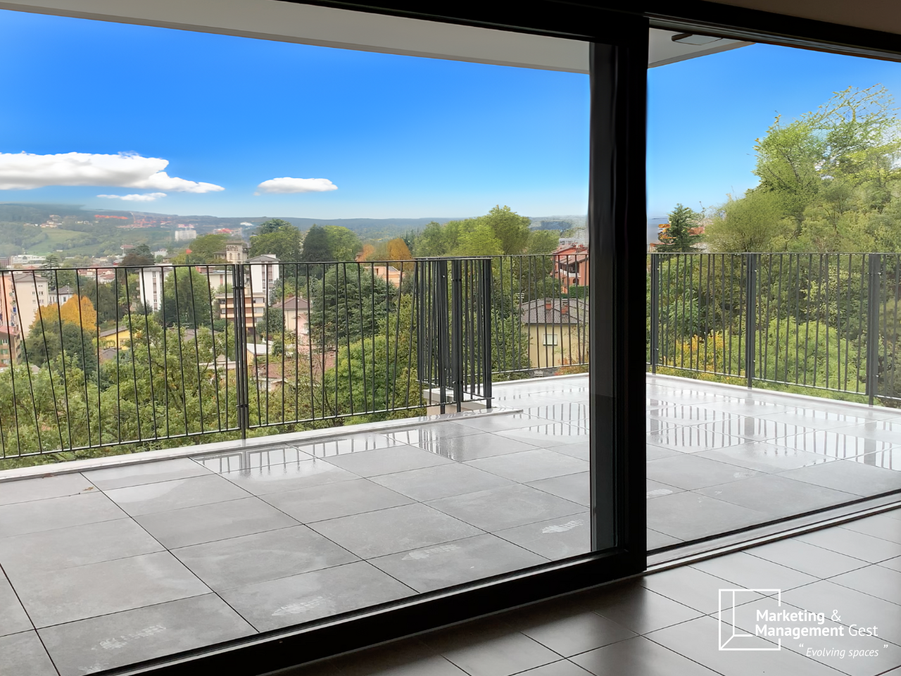 Terrace with a metal railing, tile flooring, expansive city view, greenery in the background
