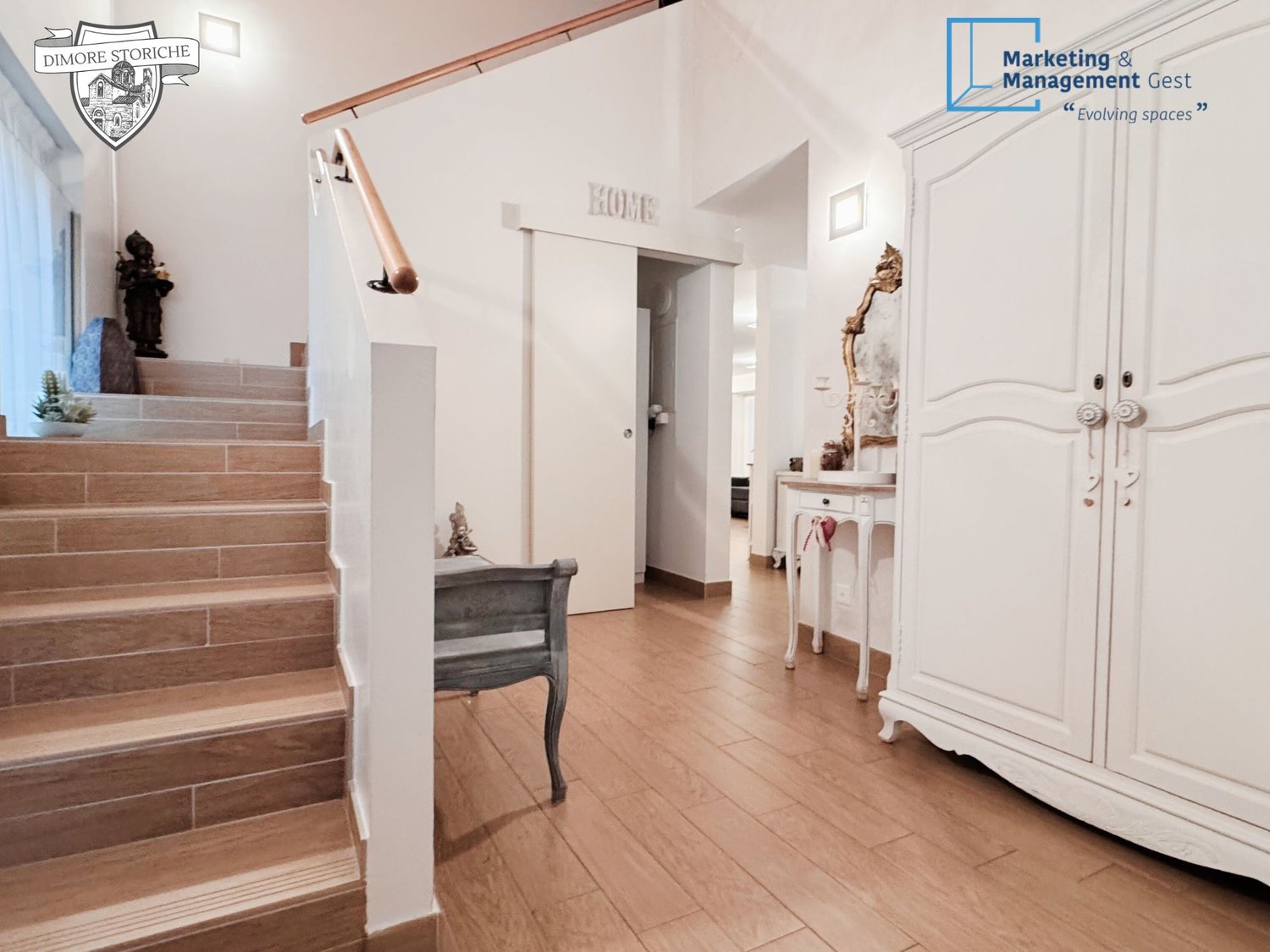 Entrance hall with wooden floor, staircase with tiled steps, decorative items, and furniture