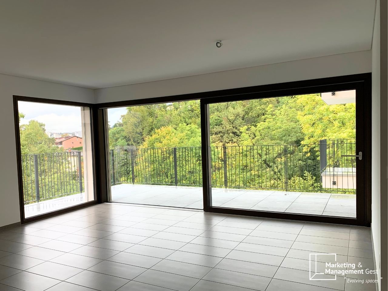 empty room with large glass doors leading to a balcony, tiled floor, white walls