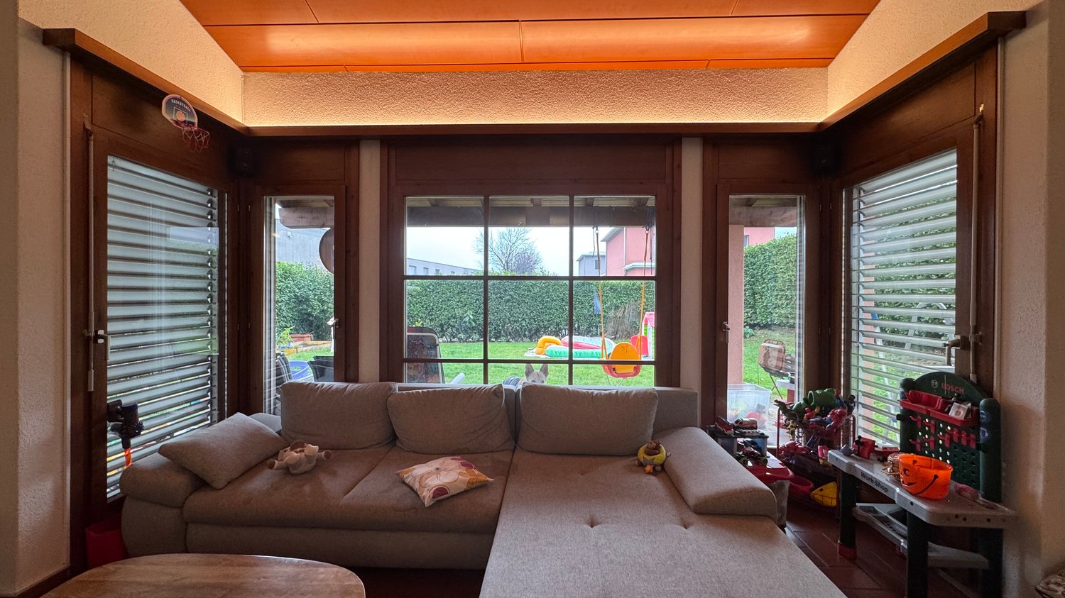 Large sofa facing window, wooden desk, toys and outdoor playground visible