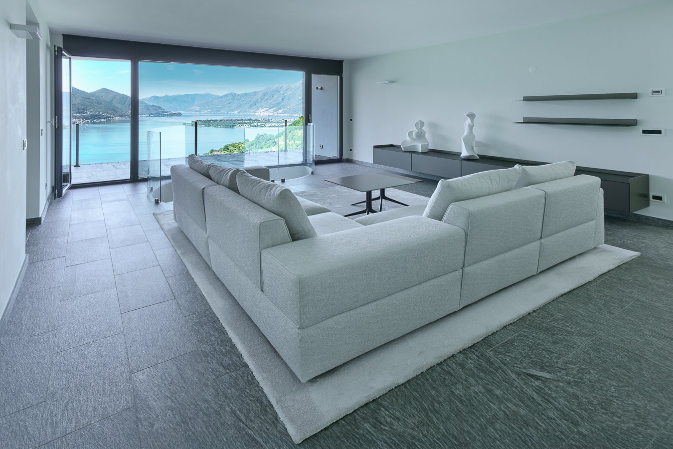 large windows, couch, glass coffee table, shelves, decorative objects, flooring