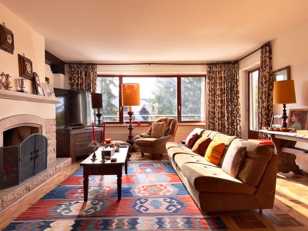 Fireplace, large windows, couch, coffee table, armchair, TV, rug, lamps, picture frames, decorative items