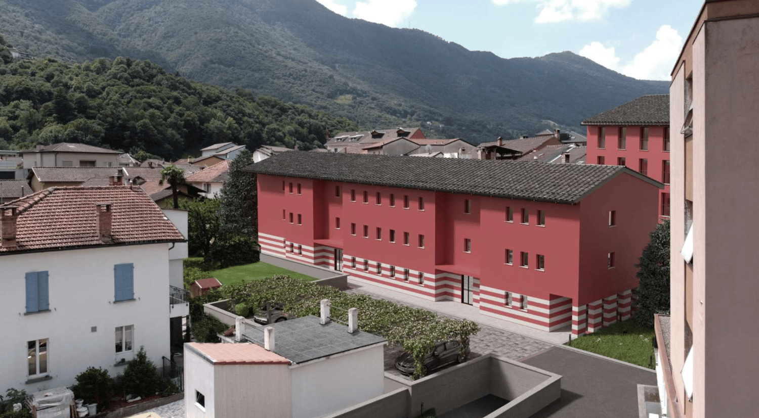 A multi-story apartment building with a red and white striped exterior, surrounded by other residential buildings and mountains in the background. There appears to be a parking area in front of the building.