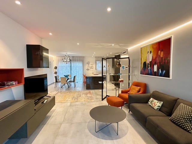 Modern and bright living room with a sofa, coffee table, flat screen TV, and paintings on the wall