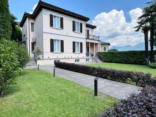 2-story house with white exterior, red roof, and balconies, surrounded by a well-maintained garden with a paved walkway.