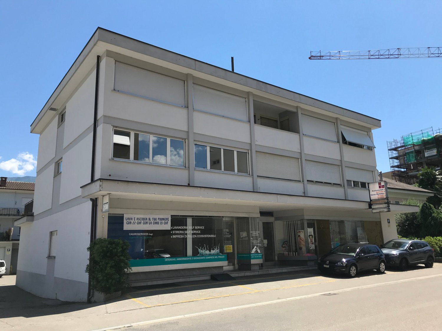 Two story white building, large windows, storefront with glass door and large window, cars parked in front