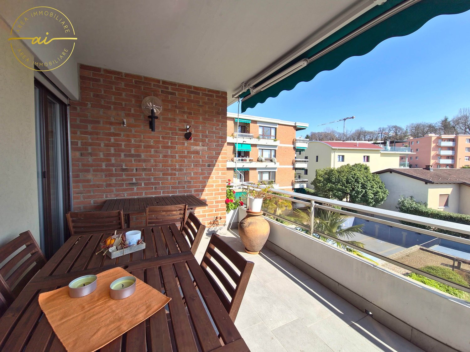 outdoor table and chairs, brick wall, awning, large vase, flowers, metal railing, tree, distant building