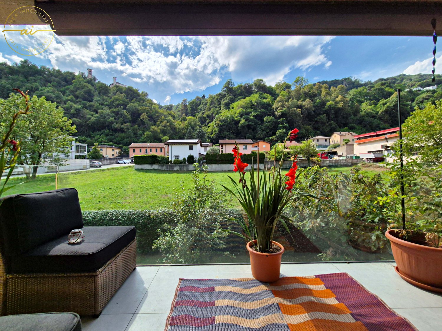 Balcony with patio, chair, plants, rug, and a view of a grassy field and hills