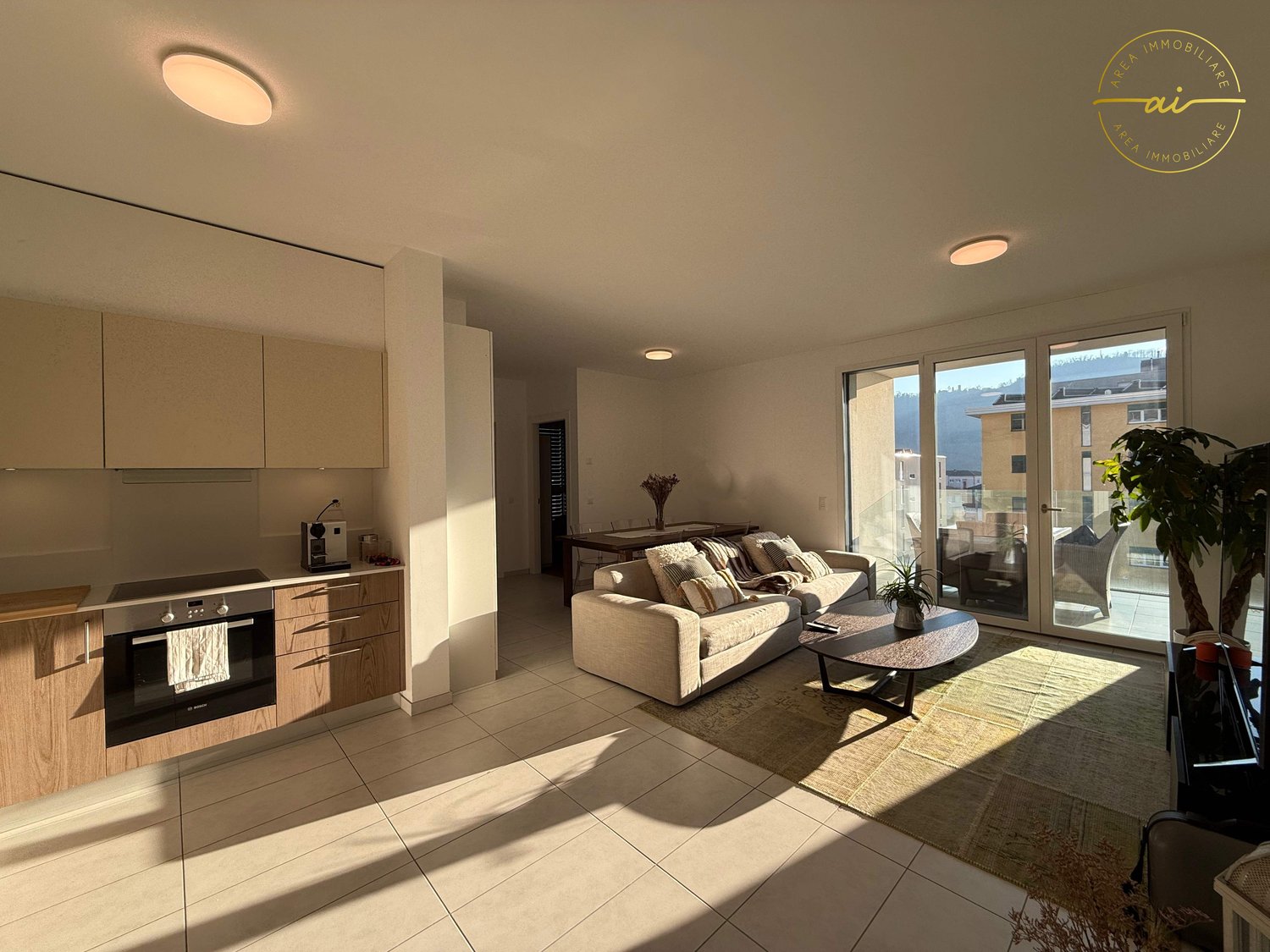 Modern kitchen and living area with sliding doors, kitchen has wooden cabinets and oven, living room has couch and coffee table, tiled floor