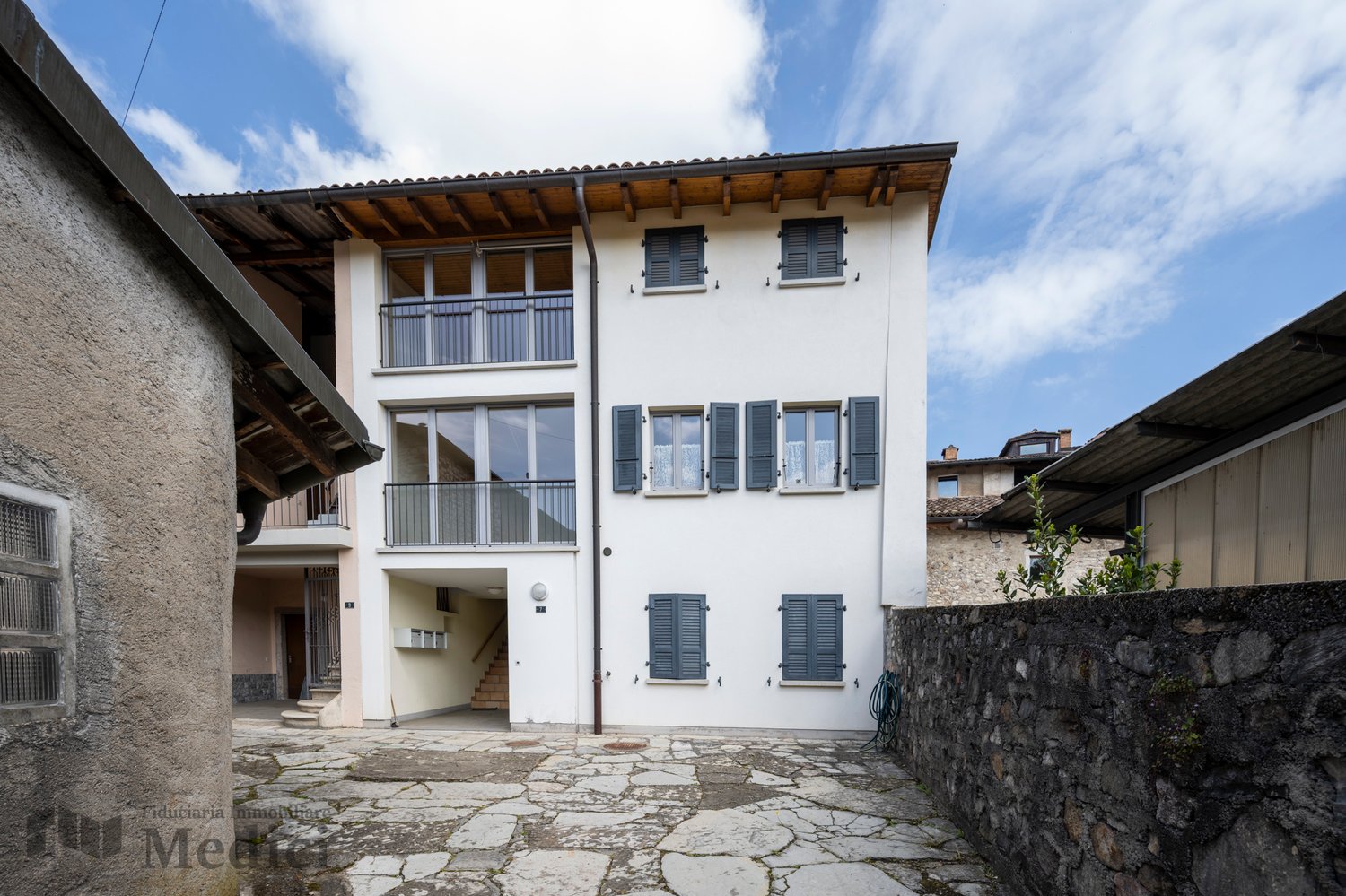 white building, 3 floors, multiple windows, balconies, stone pathway, stone wall