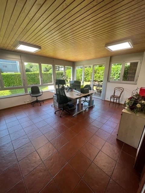 Spacious office with large windows, wooden ceiling, tiled flooring, office desk and chairs, and a cozy seating area.