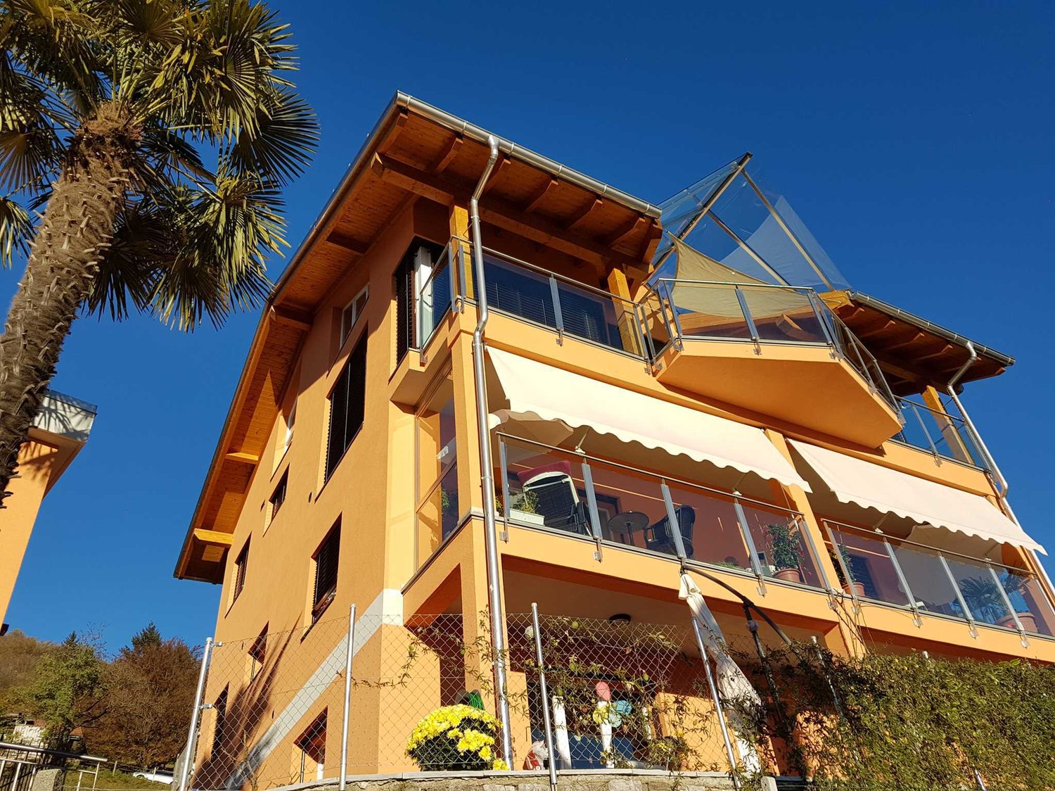 3 story house, yellow exterior, multiple balconies, glass railings, awnings, fenced yard