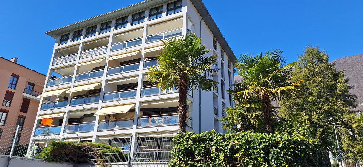 Multi-story apartment building with balconies, surrounded by palm trees and greenery