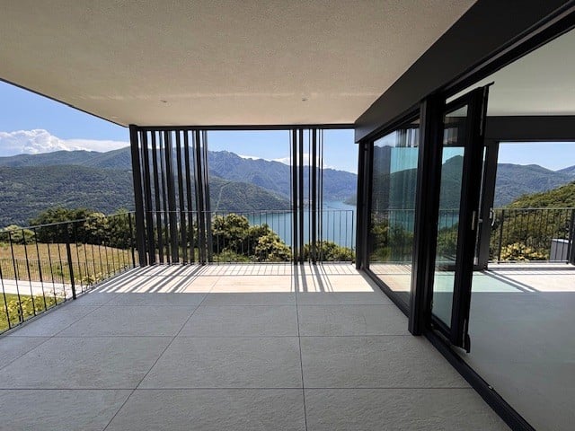 Large glass windows and sliding doors overlooking a scenic lake and mountain landscape, with a spacious outdoor terrace or balcony area.