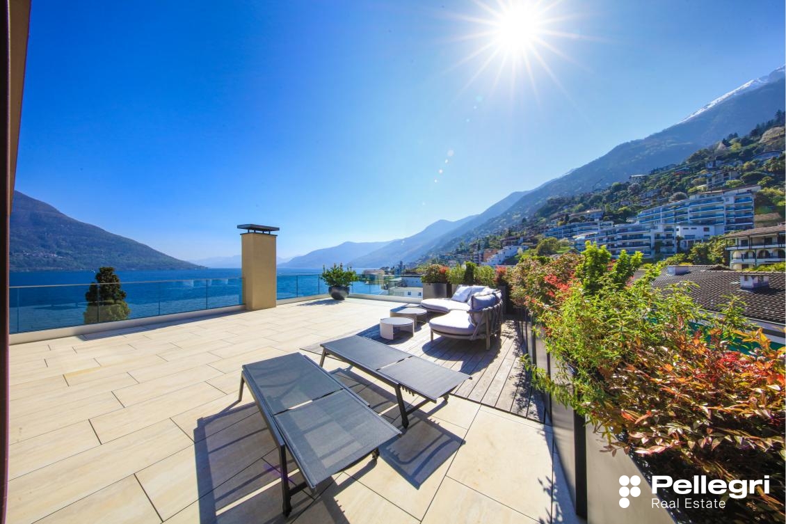 Spacious balcony or terrace with stunning views of the mountains and lake, outdoor seating area, glass railing, and lush greenery surrounding the property.