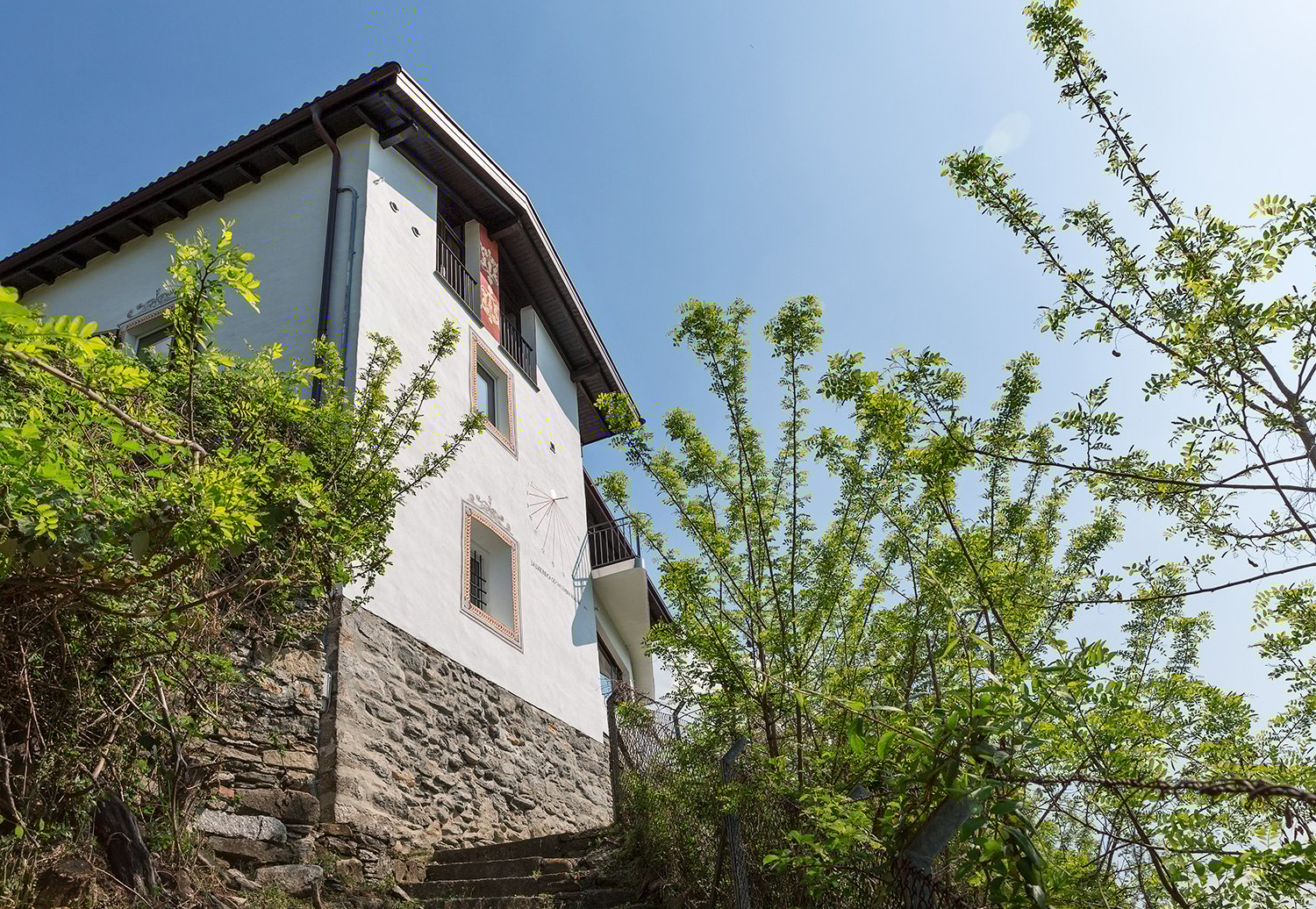 Two-story house, white wall, brown roof, stone walls, balcony, stairs