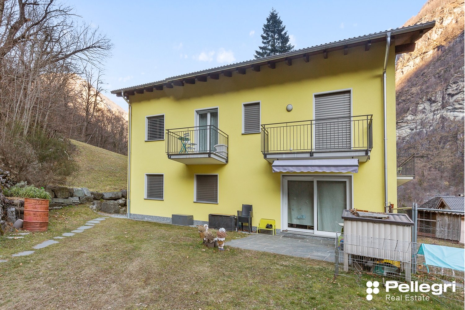 2-story yellow house, balconies, garden, mountains in the background