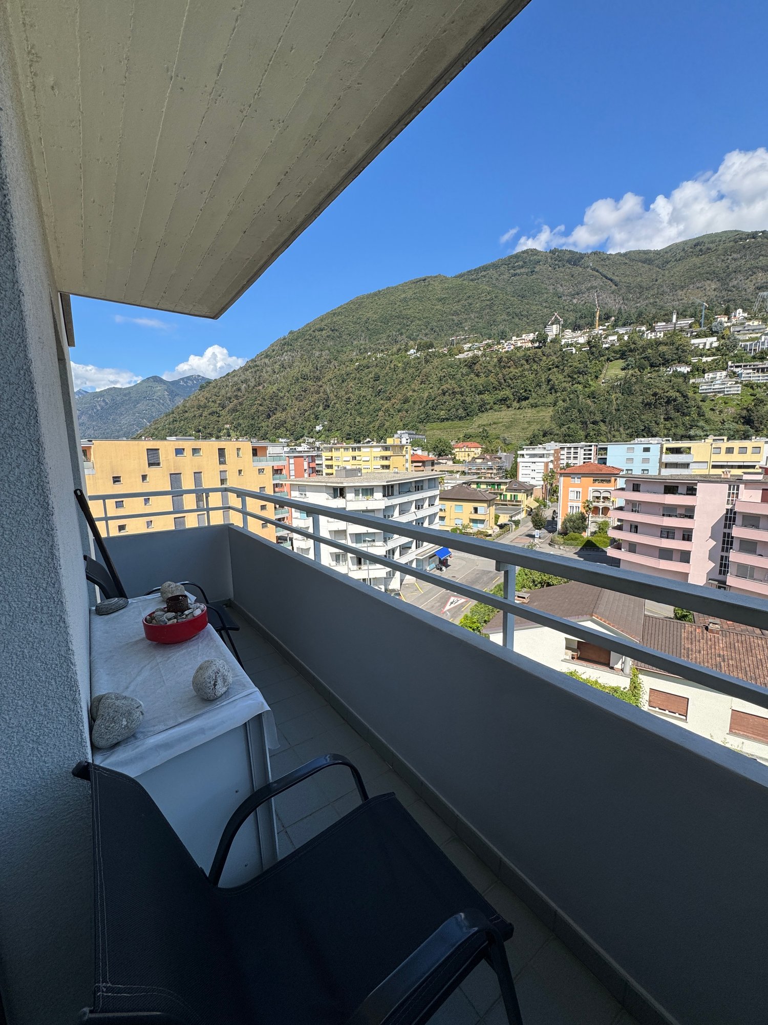 Terrace with chairs, table, and a scenic view of mountains and a town.