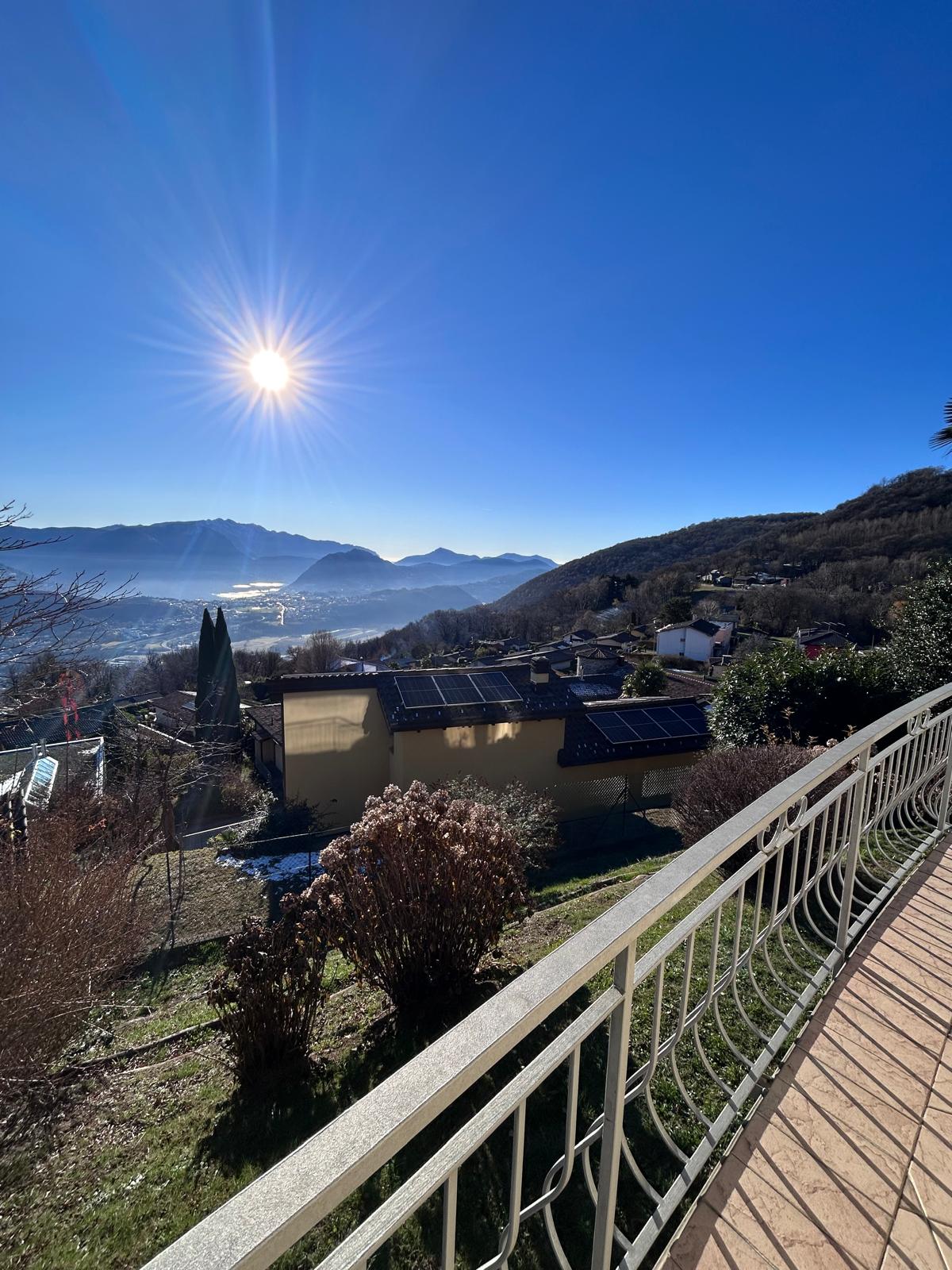 Terrace, sunlight, metal railing, tiled flooring, solar panels on a house, mountains in the distance