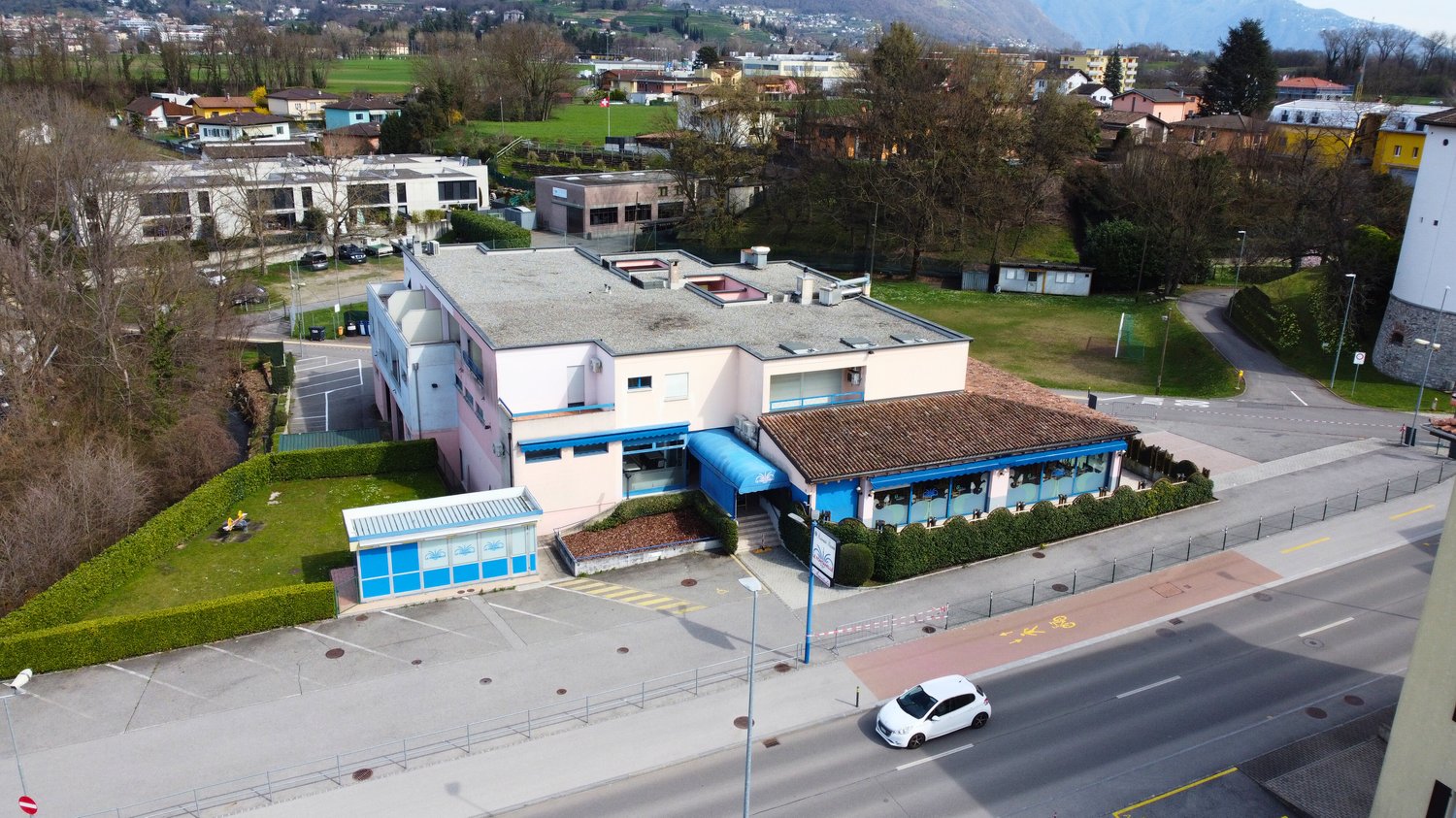2 story building, pink and brown exterior, blue awning, parking lot, trees