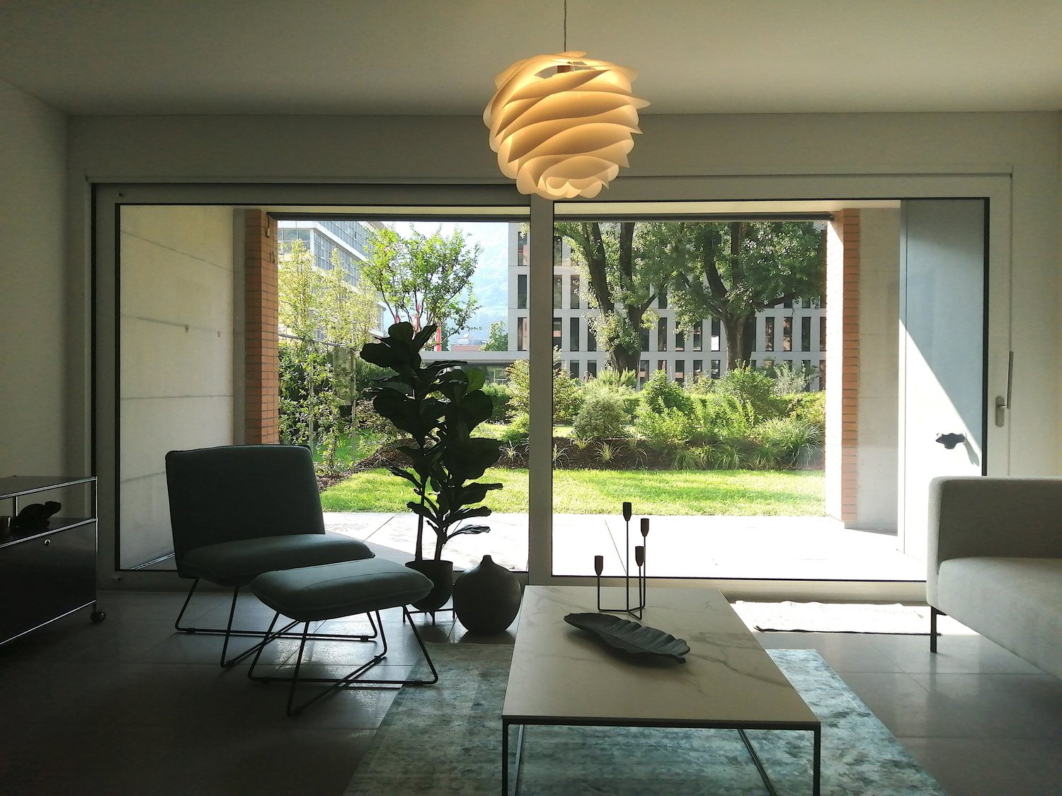 modern living room with sliding glass doors, large windows, modern furniture, plants, marble coffee table, rug, lamp