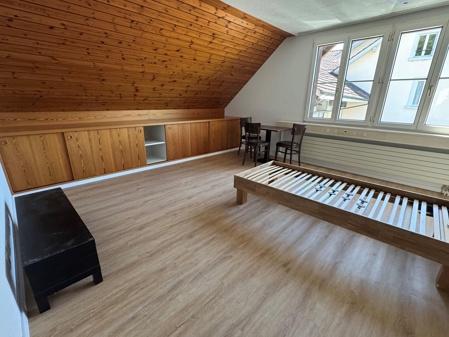 Attic room with wooden paneled walls and ceiling, hardwood flooring, large windows, built-in storage cabinets, and a piano or keyboard.