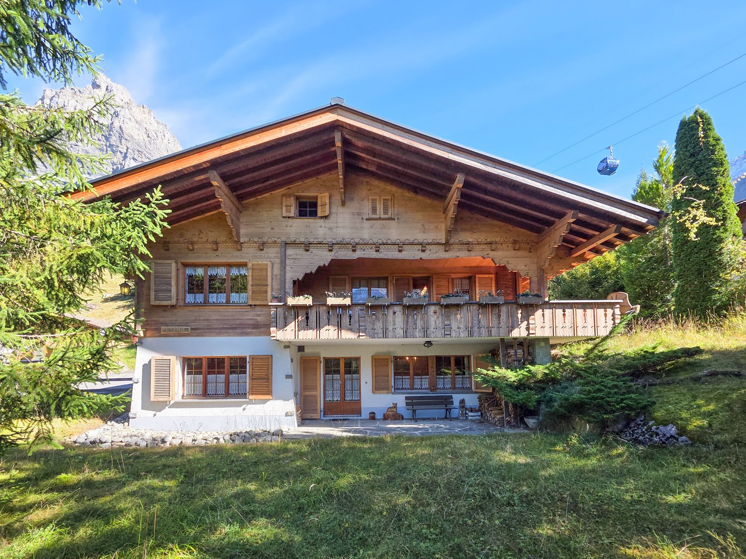 large chalet, wooden exterior, wooden roof, balcony, large windows, located on mountain slope