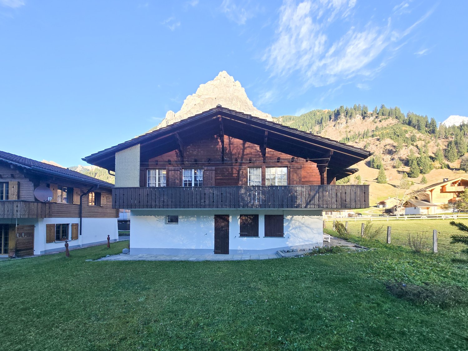 Detached house, brown wooden exterior, white painted lower level, steep slope behind, balcony on the second floor