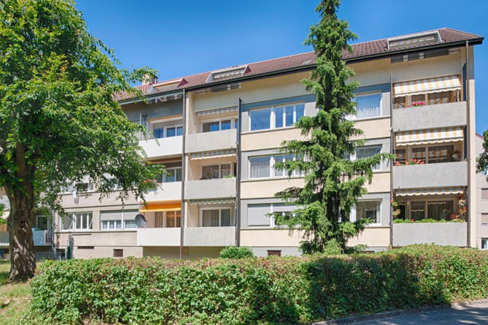 4 story building, beige, multiple balconies, trees, bushes
