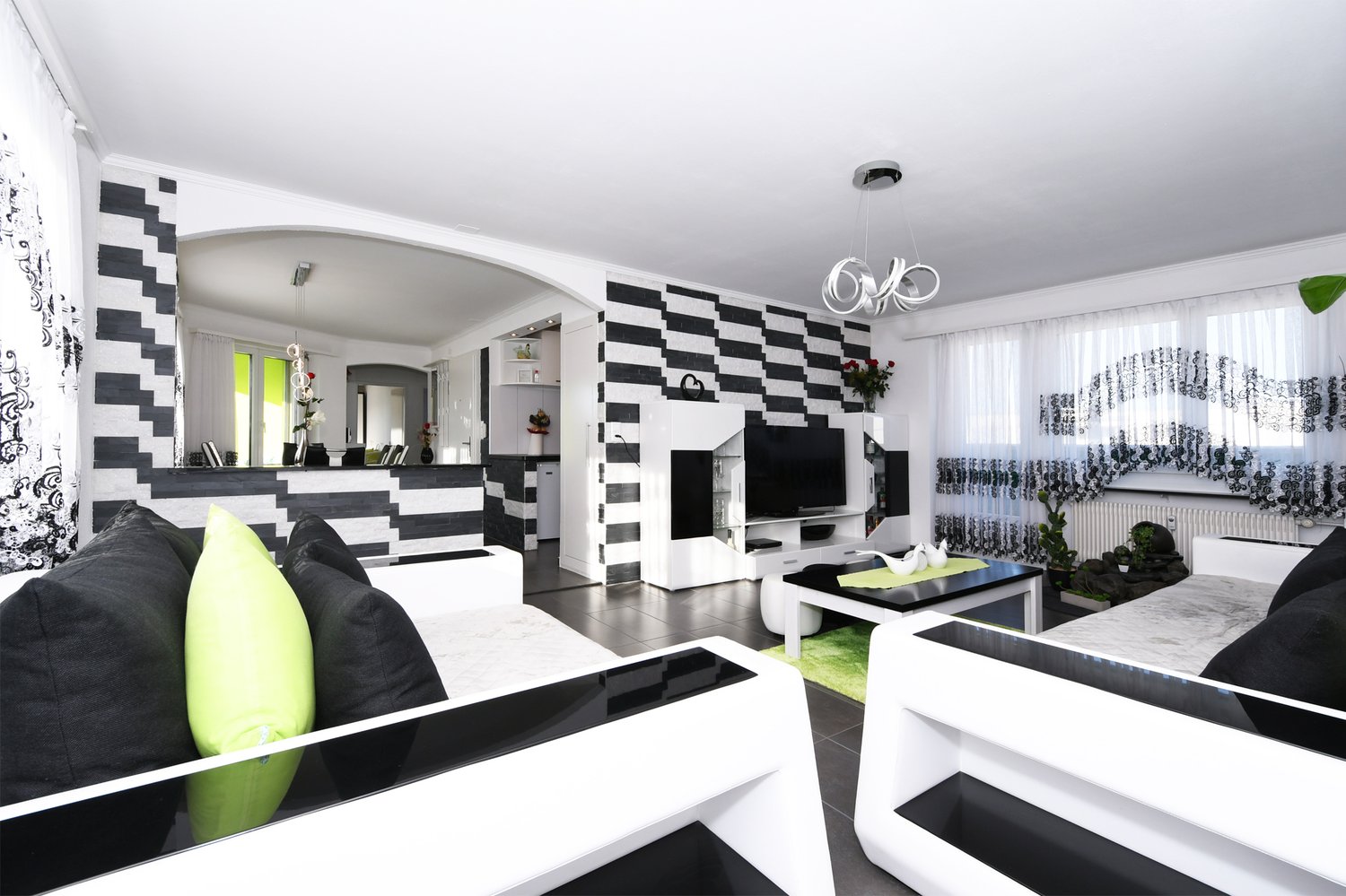 modern interior, black and white striped walls, black and green pillows, center table, sofa, white marble flooring, hanging ceiling lamp, TV
