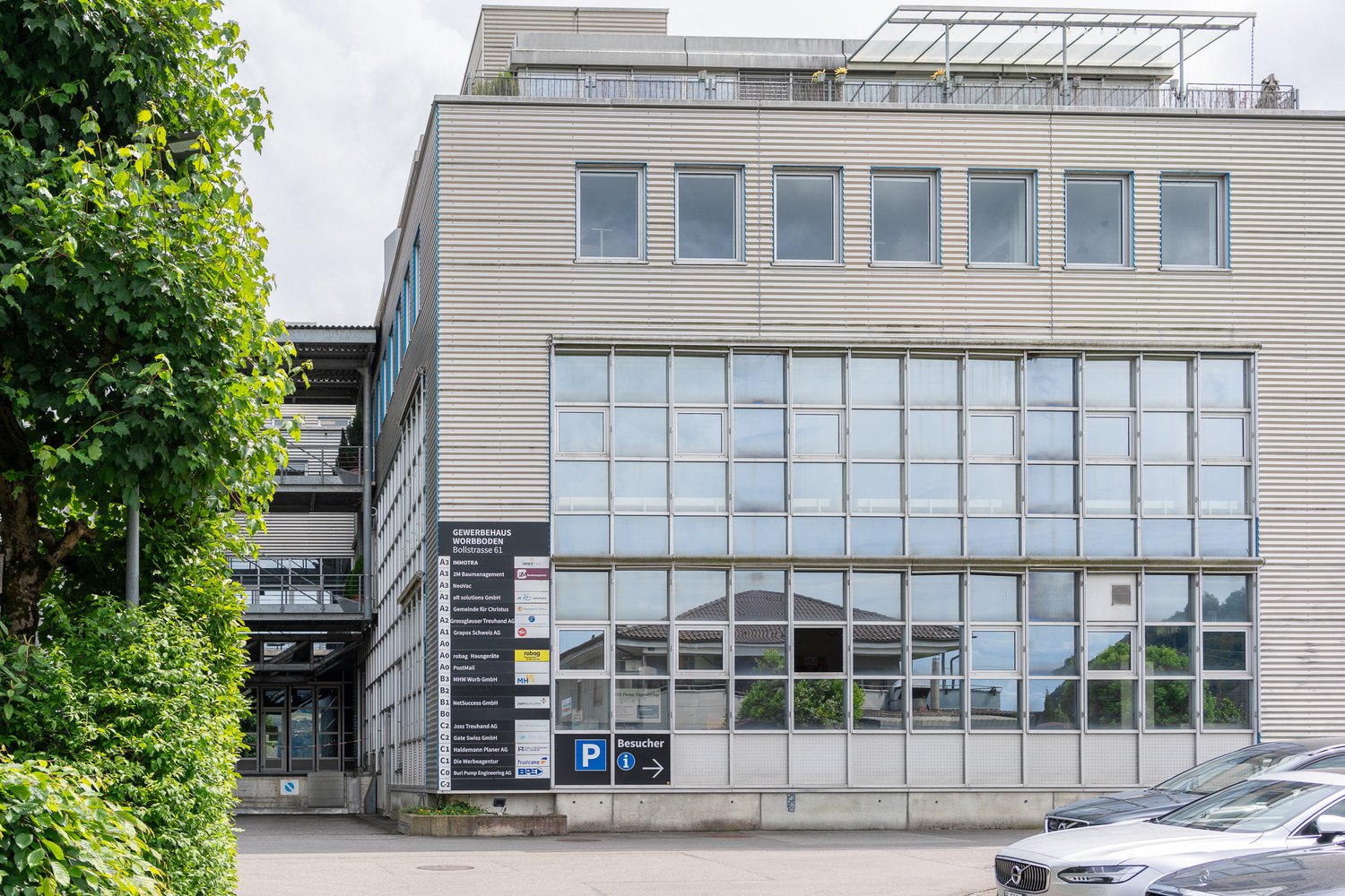 4-story commercial building with a glass facade, balconies on the top floor, and a parking area in front of the building