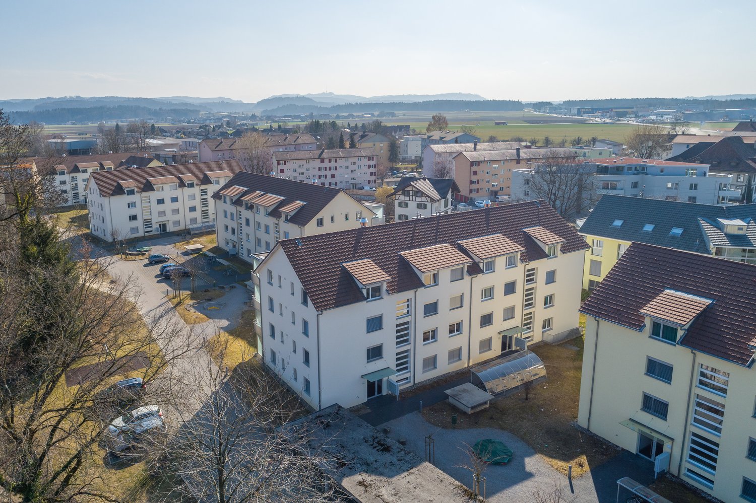 Aerial view of multiple multi-story buildings with several parking spaces and open land.